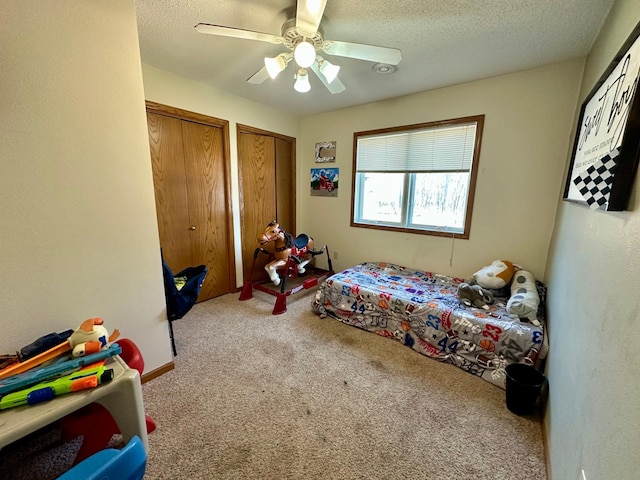 carpeted bedroom with a textured ceiling, a ceiling fan, and two closets