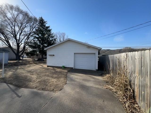 view of property exterior with an outdoor structure, concrete driveway, fence, and a detached garage