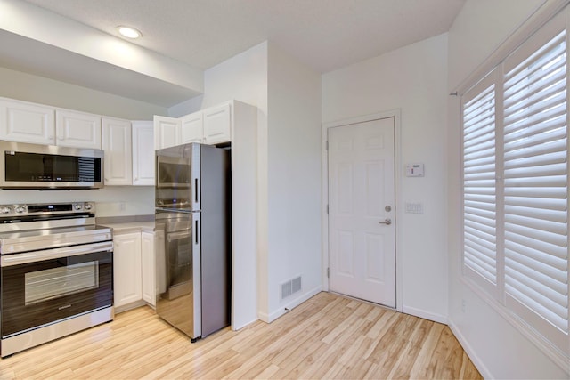 kitchen featuring baseboards, visible vents, stainless steel appliances, white cabinetry, and light wood-type flooring