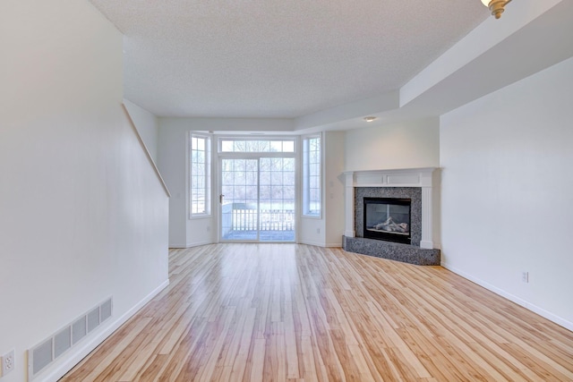 unfurnished living room with visible vents, a textured ceiling, a glass covered fireplace, wood finished floors, and baseboards