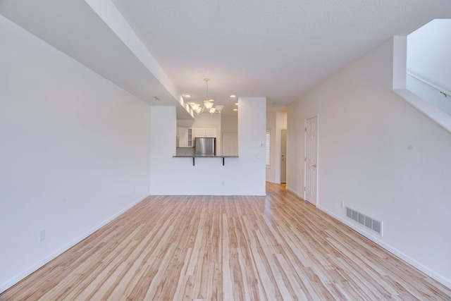 unfurnished living room featuring light wood-style flooring, a notable chandelier, baseboards, and visible vents