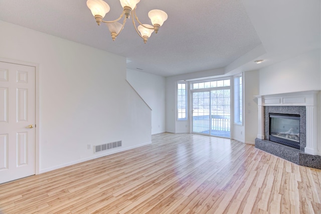 unfurnished living room featuring visible vents, baseboards, a chandelier, a premium fireplace, and light wood-style floors