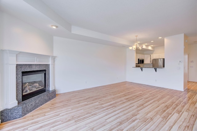 unfurnished living room with a chandelier, recessed lighting, light wood finished floors, and a fireplace