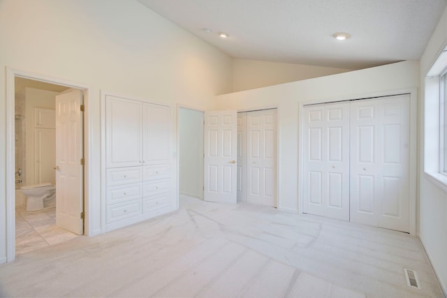 unfurnished bedroom featuring light colored carpet, connected bathroom, lofted ceiling, and multiple closets