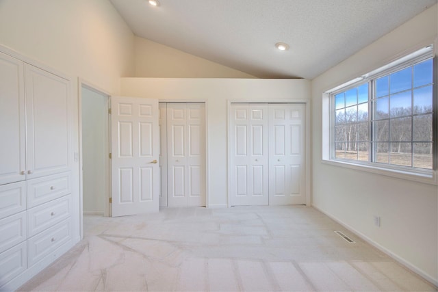 unfurnished bedroom featuring visible vents, light carpet, two closets, baseboards, and vaulted ceiling