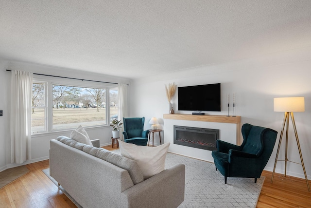 living area with a glass covered fireplace, wood finished floors, baseboards, and a textured ceiling