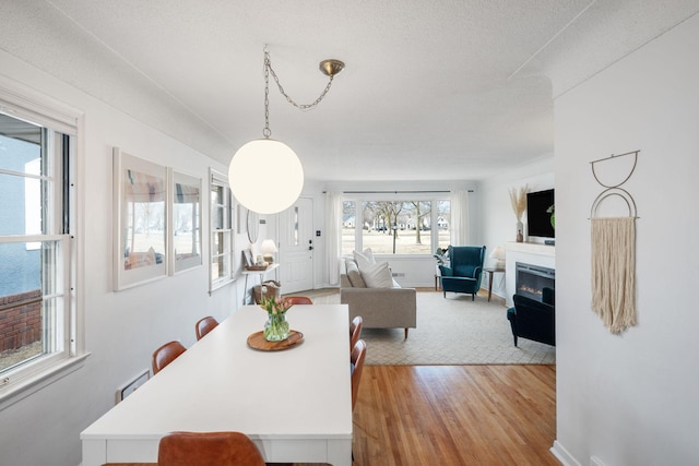 dining space featuring baseboards, light wood-style floors, and a glass covered fireplace