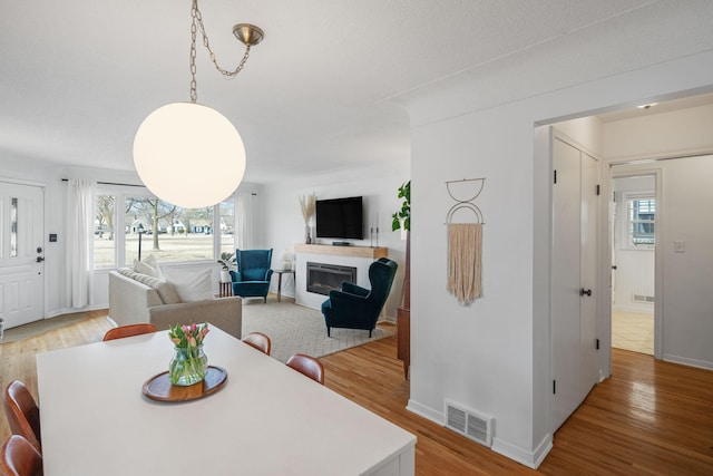 dining space featuring visible vents, baseboards, light wood-style floors, and a glass covered fireplace