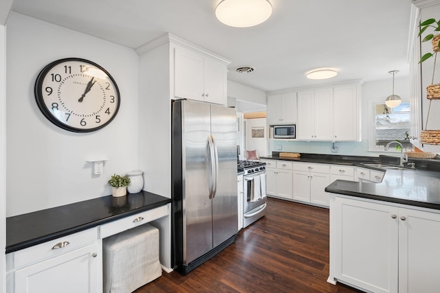 kitchen with dark countertops, dark wood-type flooring, white cabinets, stainless steel appliances, and a sink