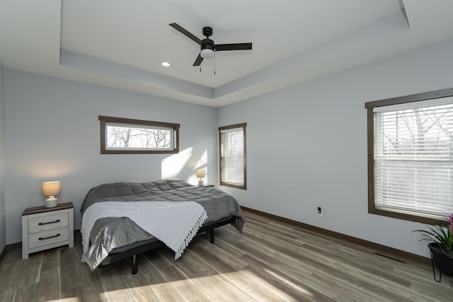 bedroom featuring a tray ceiling, baseboards, wood finished floors, a ceiling fan, and recessed lighting