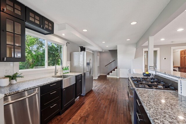 5446 Bartlett Blvd, Mound, MN 55364 - kitchen with stainless steel appliances, light stone countertops, dark wood finished floors, glass insert cabinets, and dark cabinets