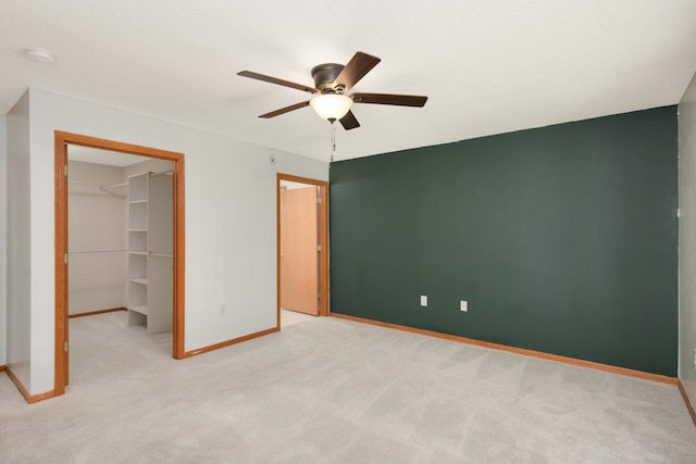 unfurnished bedroom featuring baseboards, a spacious closet, light carpet, a closet, and a ceiling fan