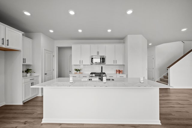 1520 Philipp Way, Shakopee, MN 55379 - kitchen featuring stainless steel microwave, a kitchen island with sink, white cabinets, wood finished floors, and decorative backsplash