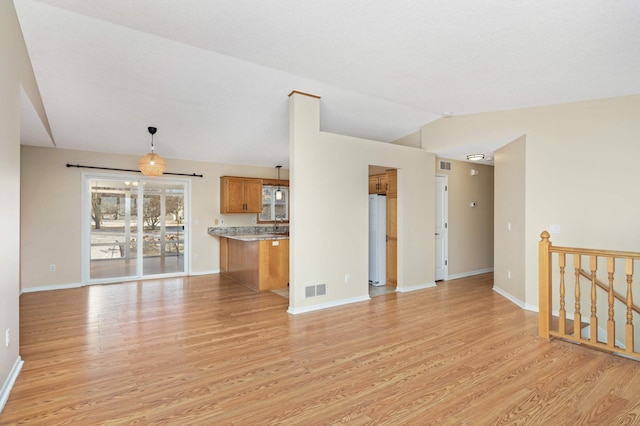 unfurnished living room featuring light wood-type flooring, visible vents, baseboards, and vaulted ceiling