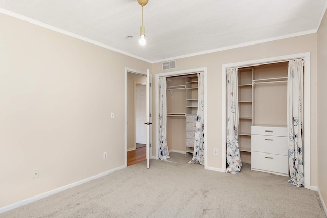 unfurnished bedroom with ornamental molding, carpet, visible vents, and multiple closets
