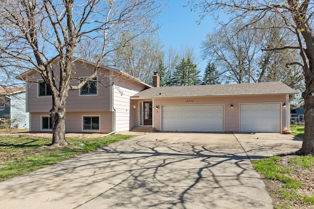 split level home with an attached garage, driveway, and a chimney