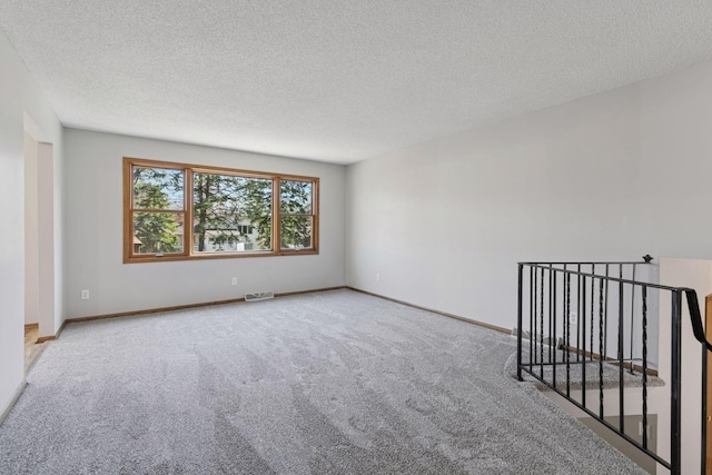 spare room featuring visible vents, a textured ceiling, carpet, and baseboards