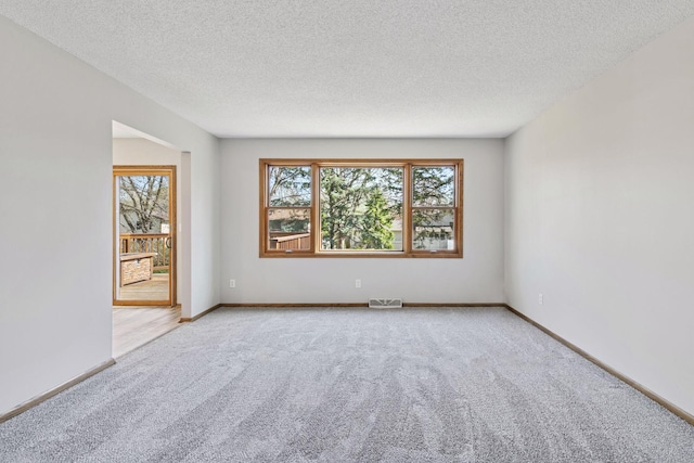 spare room with baseboards, light carpet, a textured ceiling, and visible vents