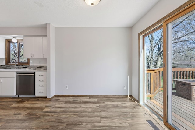 kitchen featuring stainless steel dishwasher, wood finished floors, a sink, light countertops, and white cabinetry