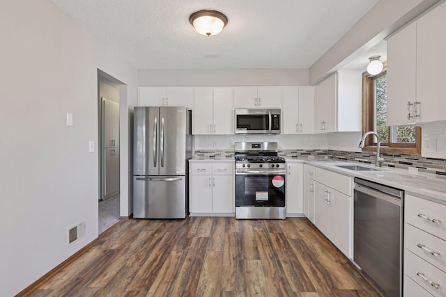 kitchen with dark wood-style flooring, appliances with stainless steel finishes, a sink, backsplash, and visible vents