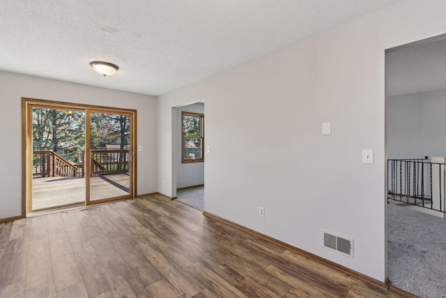 spare room featuring wood finished floors, baseboards, a textured ceiling, and visible vents