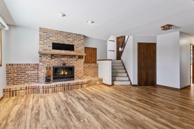 unfurnished living room featuring a brick fireplace, wood finished floors, baseboards, stairway, and a textured ceiling