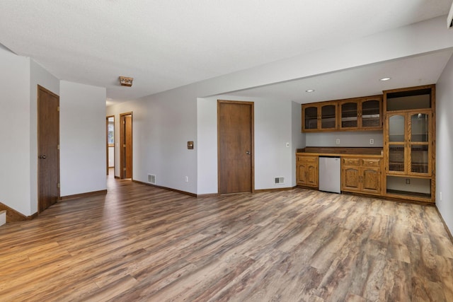 unfurnished living room with baseboards, light wood-type flooring, wet bar, and visible vents