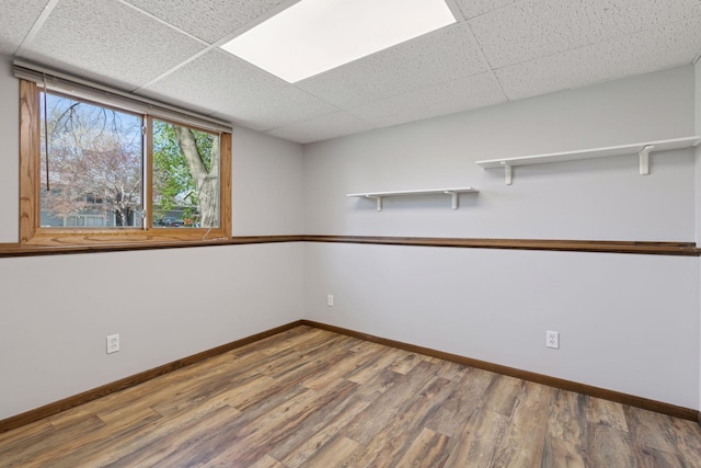 unfurnished room featuring baseboards, a drop ceiling, and wood finished floors
