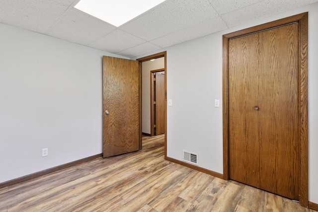 unfurnished bedroom featuring baseboards, visible vents, a paneled ceiling, and light wood-style floors