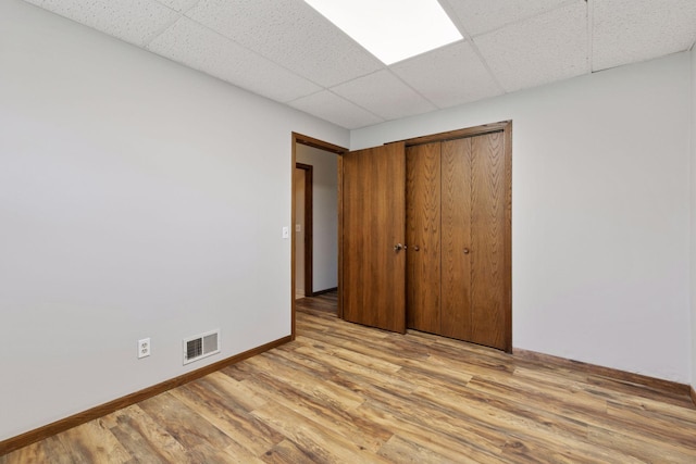 unfurnished bedroom featuring visible vents, light wood-type flooring, baseboards, a closet, and a drop ceiling