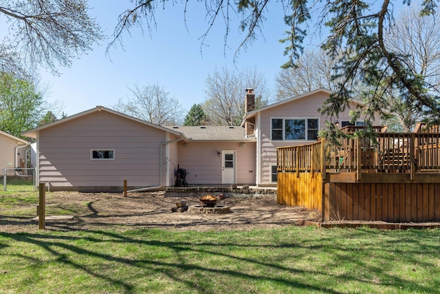 back of property with a chimney, a deck, fence, an outdoor fire pit, and a yard