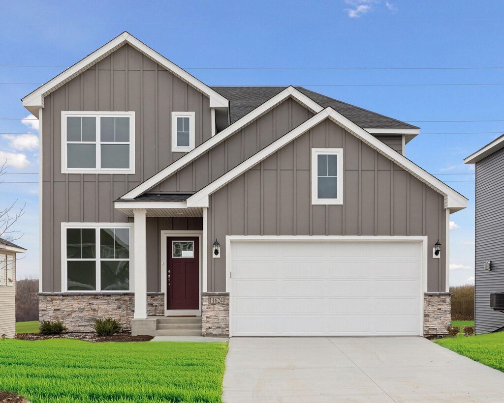 view of front of home featuring driveway, stone siding, board and batten siding, a front yard, and a garage