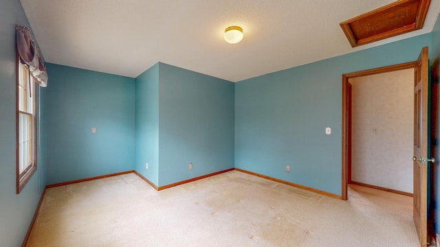 spare room featuring baseboards, light colored carpet, and attic access