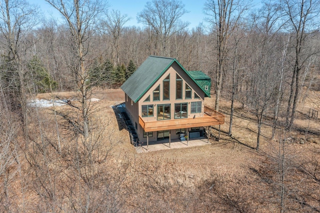 back of house with a wooded view, a patio, and a deck
