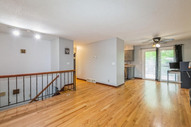unfurnished living room with light wood-type flooring, a ceiling fan, rail lighting, a textured ceiling, and baseboards