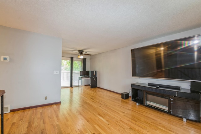 unfurnished living room with wood finished floors, ceiling fan, baseboards, and a textured ceiling