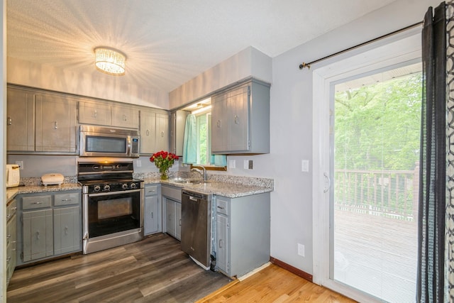 kitchen with stainless steel appliances, gray cabinets, a sink, and dark wood-type flooring