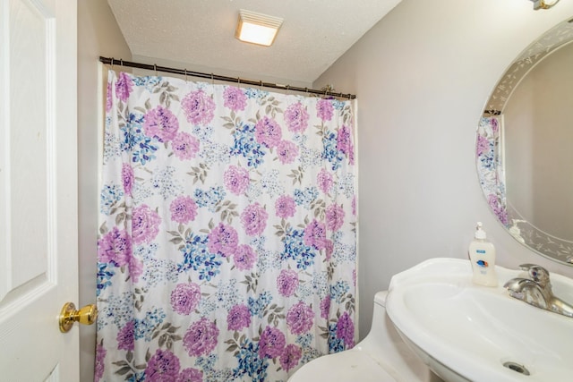 bathroom featuring a sink, a shower with shower curtain, toilet, and a textured ceiling