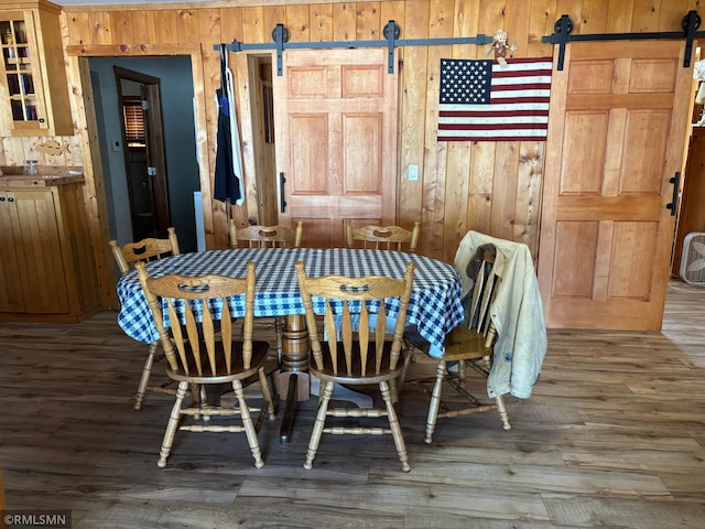 dining area featuring a barn door, wood finished floors, and wooden walls