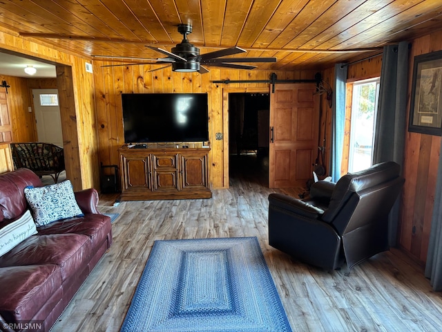 living area featuring a barn door, wood ceiling, wooden walls, ceiling fan, and wood finished floors