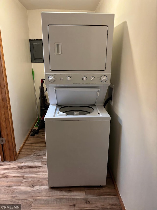clothes washing area with stacked washer and clothes dryer, light wood-style flooring, baseboards, and electric panel