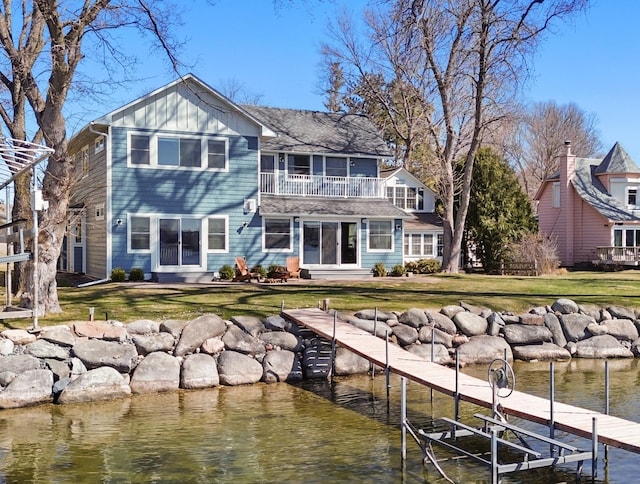 rear view of property with board and batten siding, a lawn, a water view, entry steps, and a balcony