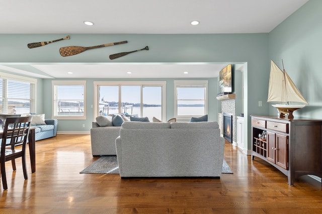 living area with wood finished floors, baseboards, a glass covered fireplace, and recessed lighting