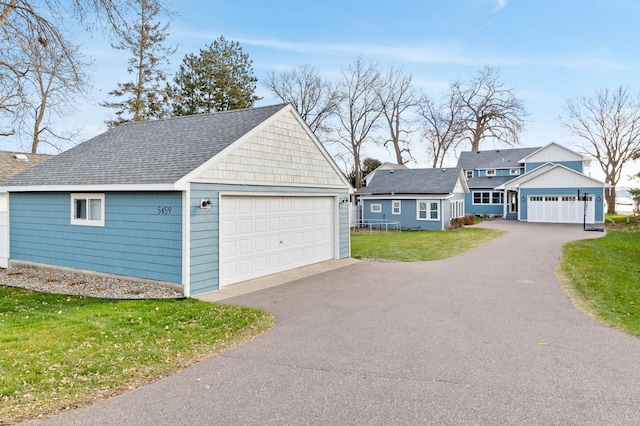 view of front of house with a shingled roof, an outbuilding, a garage, and a front yard