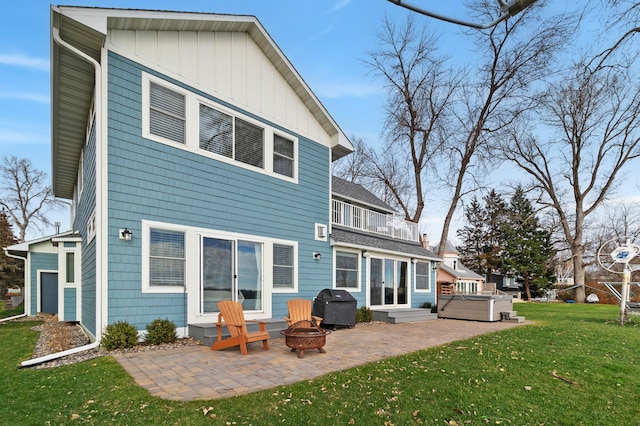 back of house with a hot tub, a patio area, a lawn, board and batten siding, and a balcony