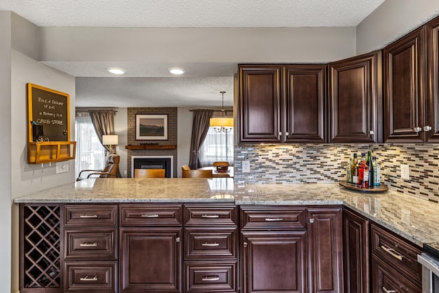 kitchen with decorative backsplash, a peninsula, dark brown cabinetry, a fireplace, and a textured ceiling