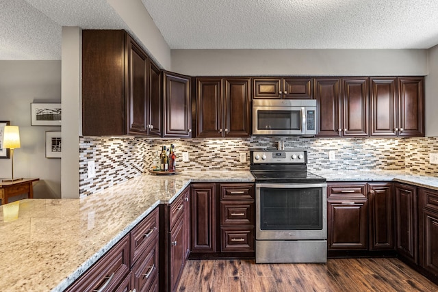 kitchen featuring stainless steel appliances, a textured ceiling, light stone countertops, and dark wood-style floors
