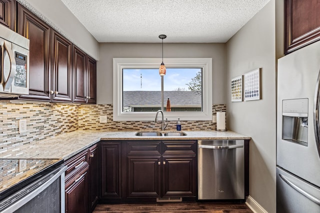 kitchen with decorative backsplash, dark wood-style flooring, dark brown cabinetry, a sink, and appliances with stainless steel finishes