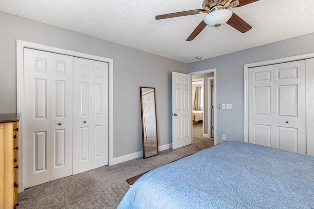 bedroom with ceiling fan, carpet floors, a textured ceiling, two closets, and baseboards