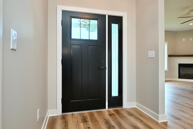 foyer entrance featuring ceiling fan, baseboards, a glass covered fireplace, and wood finished floors